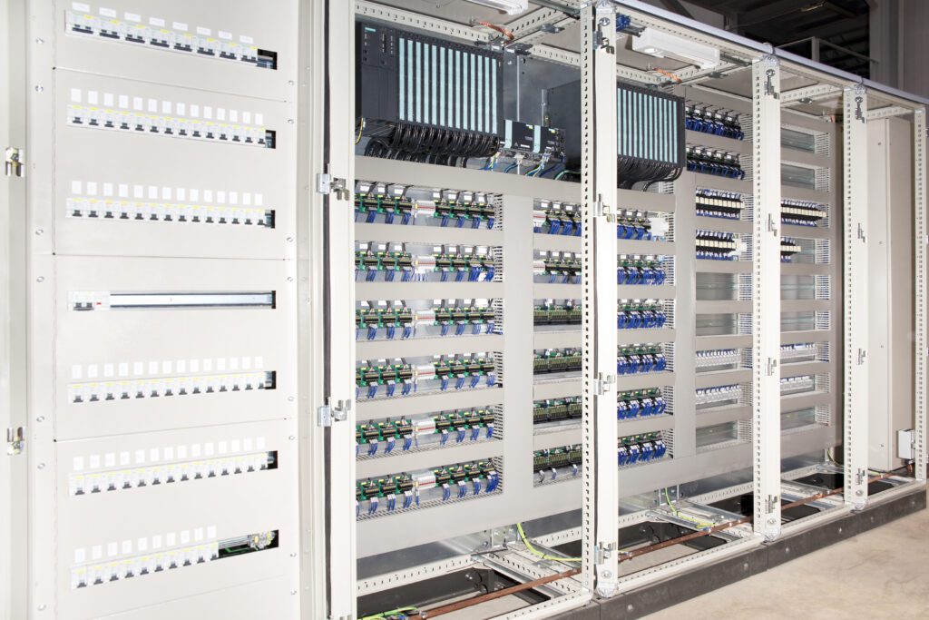 Grand panneau électrique automatisé avec modules de contrôle, rangées de disjoncteurs et borniers de câblage industriel.