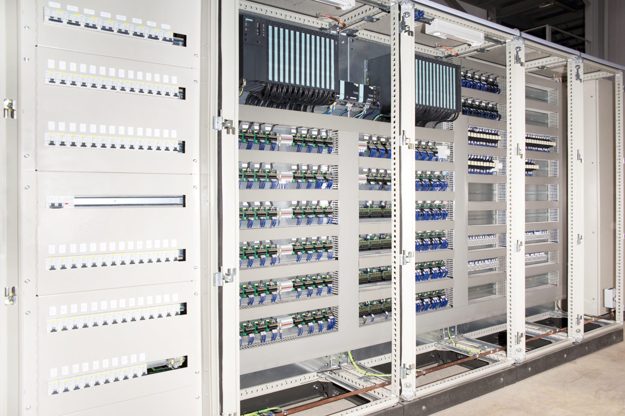 Grand panneau électrique automatisé avec modules de contrôle, rangées de disjoncteurs et borniers de câblage industriel.