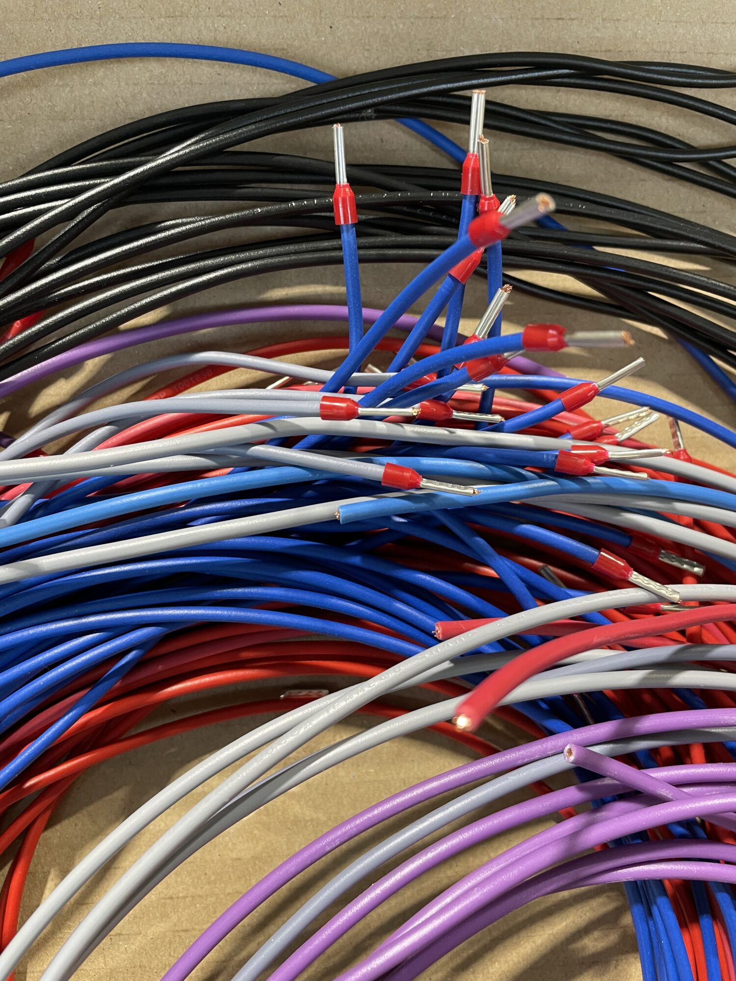 Fils électriques de différentes couleurs avec embouts rouges sertis, disposés en atelier sur un plan de travail.