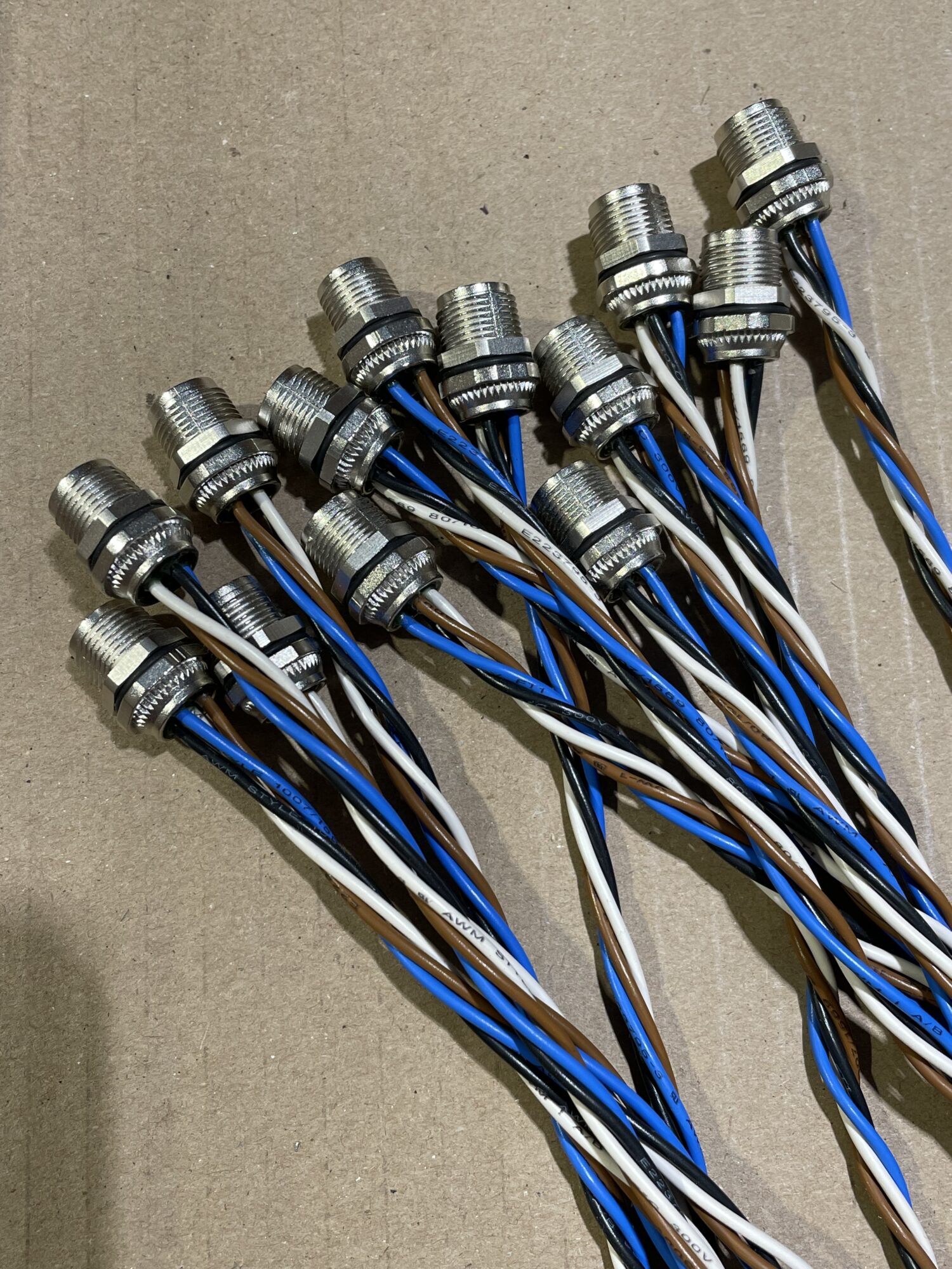 Vue rapprochée de connecteurs filetés avec fils torsadés multicolores (bleu, blanc, marron) utilisés pour le pré-câblage électrique dans un atelier industriel.