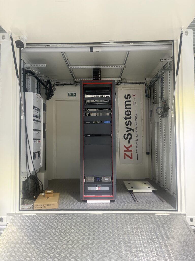 Vue intérieure d’un data center conteneurisé ZK-Systems équipé d’une baie serveur centrale, de coffrets électriques et de câblages industriels.